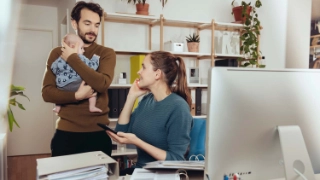 Ein junges Paar mit Kind am Reden, während die Frau im Homeoffice arbeitet.